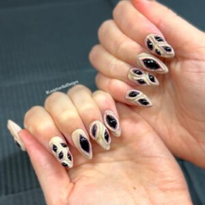 Close-up of hands wearing sculpted press-on nails designed to resemble torn skin revealing glossy black voids. The nails have a 3D texture, almond shape, and a fleshy base tone with high-contrast black center details.