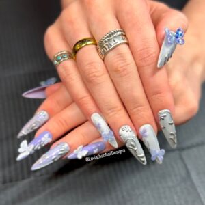 Full set of long, stiletto and coffin-shaped press-on nails in silver and lavender tones. Designs include sculpted angel wings, 3D butterflies, floral embellishments, and shimmering finishes. A mix of textures and hand-painted detailing creates a dreamy, ethereal effect.